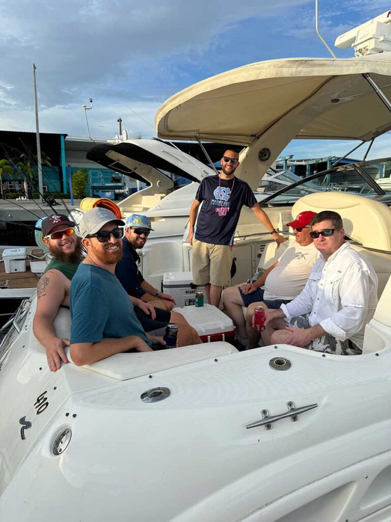 Group of men smiling and seated together on a boat, enjoying drinks at the marina.