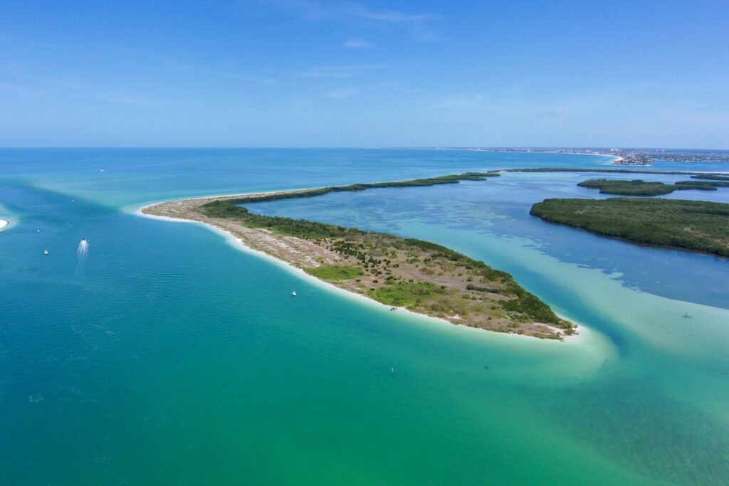 Aerial view of a small, sandy island surrounded by turquoise water and lush greenery.