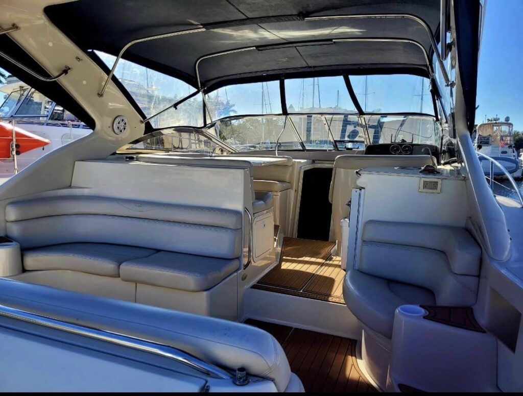 Spacious interior of a docked yacht with cushioned seating, open cockpit, and view of nearby boats.