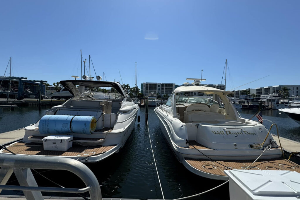 Two docked cabin cruiser boats with covered seating, one named "Well Played Days."